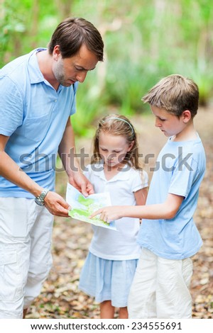 Family of father and little kids looking on map while hiking at forest or park