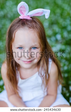 Adorable little girl wearing bunny ears in a spring garden on Easter day