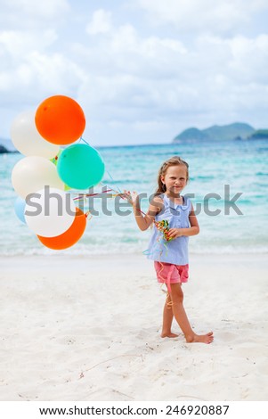 Little girl with colorful balloons at beach celebrating birthday during summer vacation