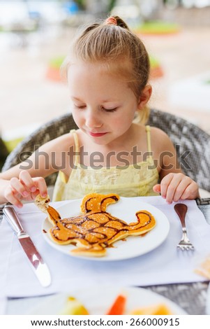 Adorable little girl eating pancake for a breakfast in restaurant