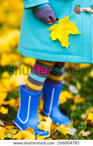 Close up of a little girl in colorful clothes and blue boots outdoors at beautiful autumn park