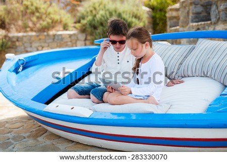 Brother and sister looking together at screen of tablet device at outdoor terrace on summer day