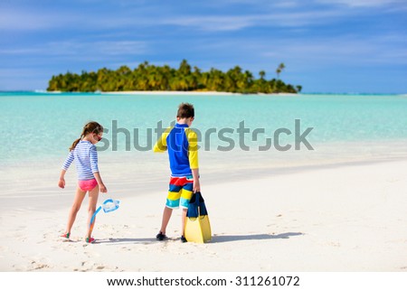 Little kids in rash guards for sun protection with snorkeling equipment on tropical beach during summer vacation