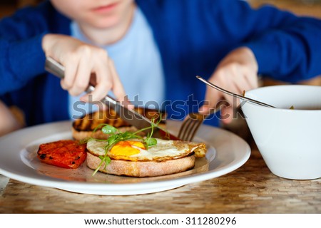 Boy eating fried egg on toast and porridge for breakfast