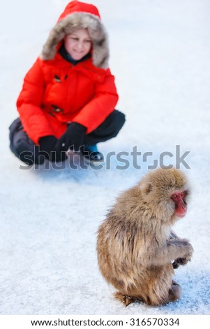 Teenage boy at Snow monkey Japanese Macaque park looking at monkey on snow in Nagano, Japan