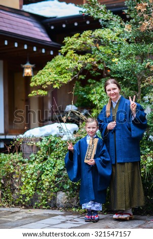 Family of mother and daughter wearing yukata at street of onsen resort town in Japan. Translation of text on wooden plate: passport for round bath visit to protect you from bad luck.