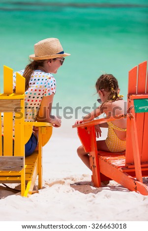 Back view of mother and daughter family sitting on colorful wooden chairs at tropical beach enjoying summer vacation