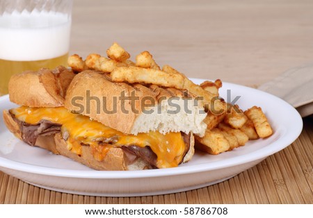Roast beef sandwich covered with melted cheese along with french fries and a beer
