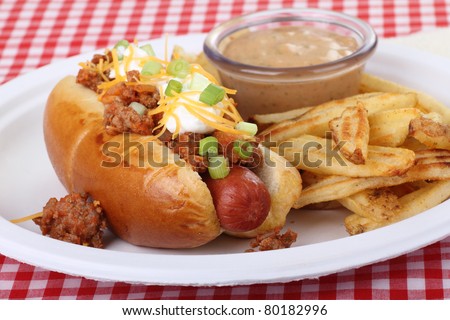 Chili hot dog with cheese and onions on a bun and french fries