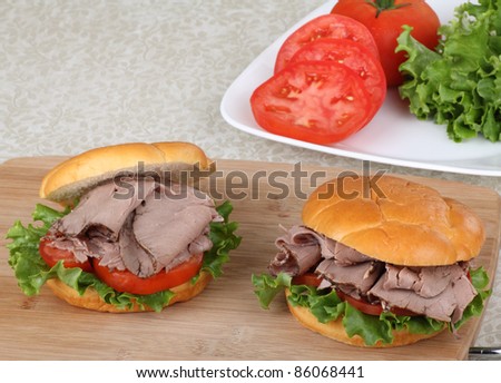 Two roast beef sandwiches on a cutting board with ingredients in background
