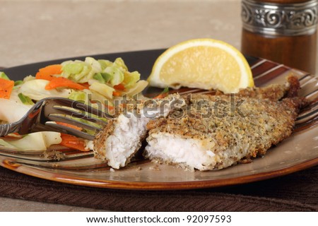 Fried catfish fish fillet with a piece on a fork with coleslaw and lemon slice