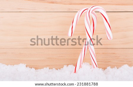 Two candy canes in snow against a wood background