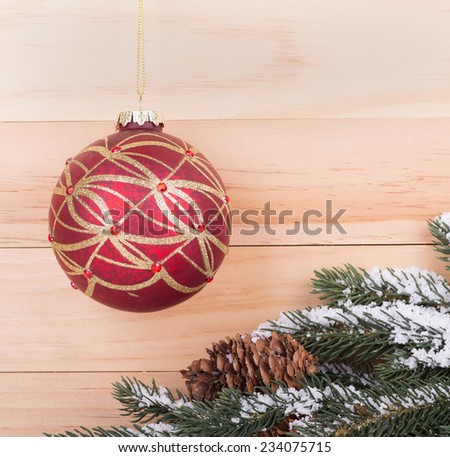 Red and gold Christmas ball with snowy evergreen tree branch against a wood background