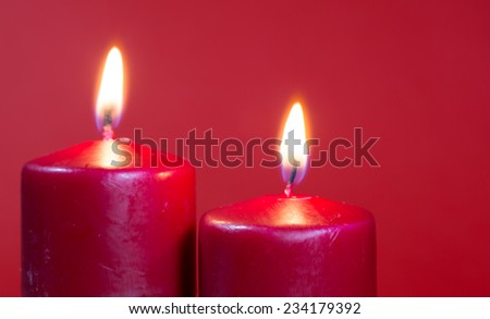 Closeup of two burning red candles against a red background