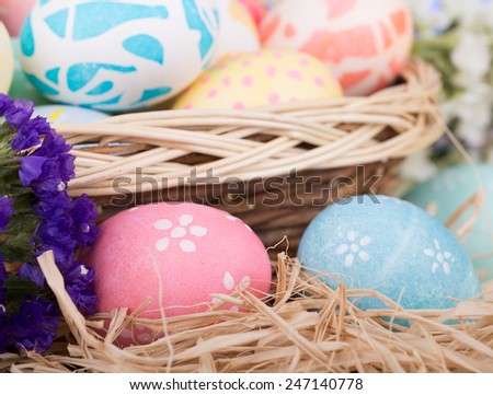 Closeup of two colored Easter eggs with a basket of eggs in back