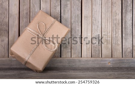Package wrapped in brown paper and string leaning against a wood fence