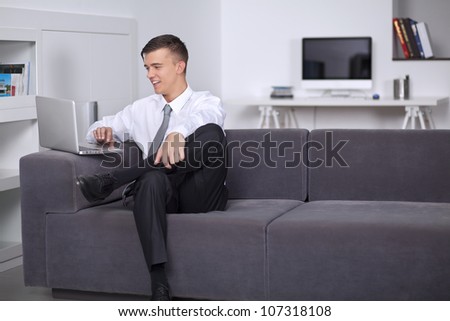 Smiling young businessman working with laptop at sofa in office sitting on couch