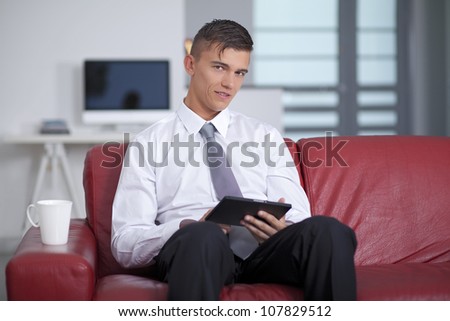 Happy young businessman holding and touching a digital tablet and sitting on couch