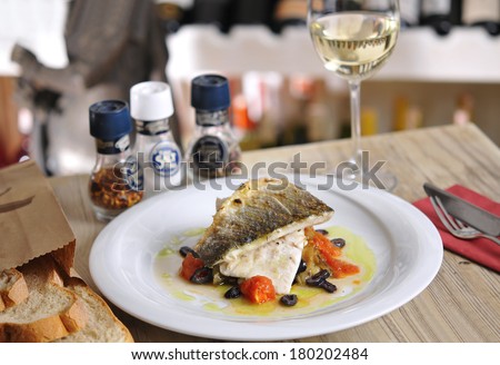 Grilled fish and garnitures in plate and white wine on wooden table