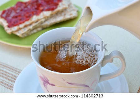pouring tea in cup with crispy bread and jam
