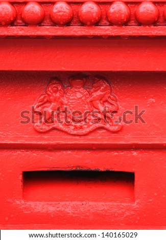 Old English red mailbox detail showing coat of arms and mail slot.