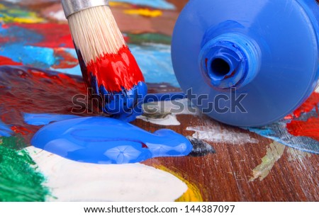 Classic artists palette and blue paint tube with paintbrush dipped in red and blue paint.