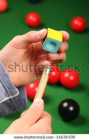 Man chalking the end his snooker cue with table and balls in background