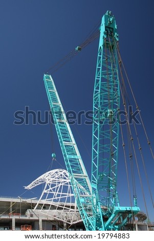 Large blue crane with new roof girder being put on for a stadium roof