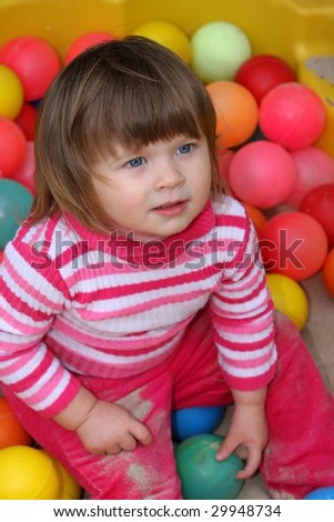 Pretty young toddler girl playing with colored balls in her sandpit