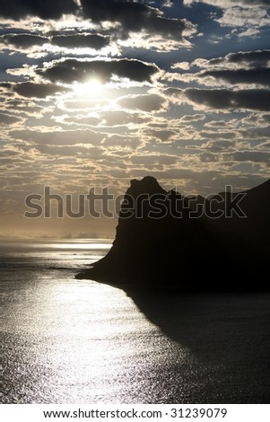 Silhouette of a mountain at the ocean and clouds in the sky