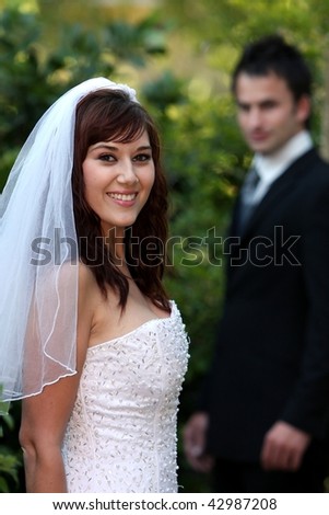 Beautiful smiling bride with her husband our of focus in the background