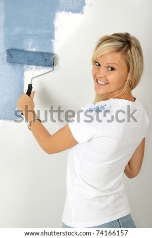Lovely young blond woman painting a wall powder blue