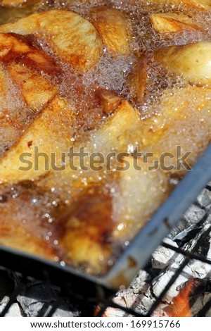 Potato wedges or chips deep frying in a pan of oil over a fire