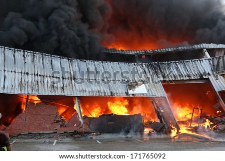Warehouse building burning with intense flames and fireman attending