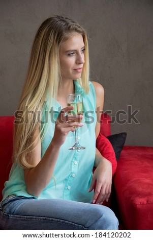 Gorgeous young blond lady enjoying a glass of wine on the red sofa