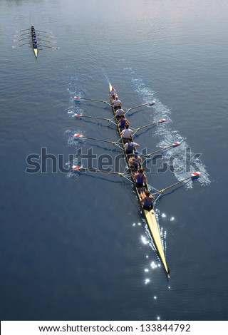 Two boats of eight men with helmsman are rowing  on a sunny day.