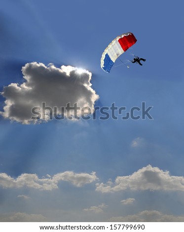 Blue, white, red sail parachute on blue sky, sun behind a cloud