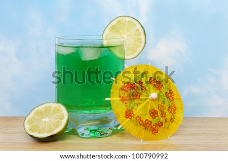 Lime flavored cocktail drink with fruit and a cocktail umbrella on a wooden surface against a blue sky