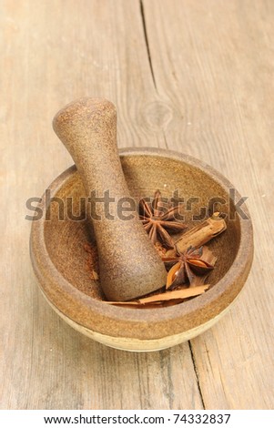 A stoneware pestle and mortar with star anise and cinnamon spices on a background of old cracked wood