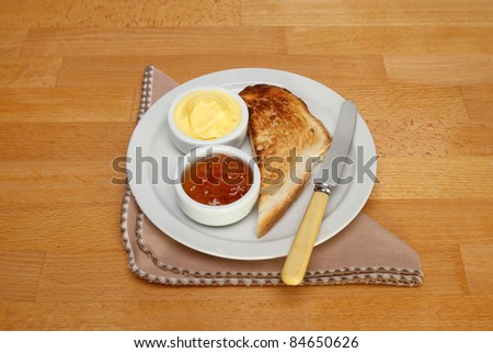 Toast, marmalade and butter on a plate with a knife and napkin upon a wooden table