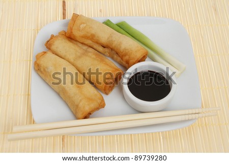 Chinese pancake rolls with spring onions and soy sauce on a plate with chopsticks on a bamboo mat
