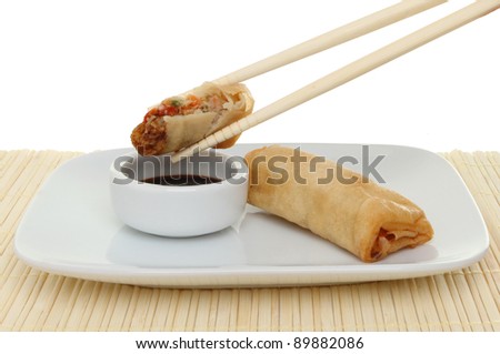 Chinese pancake roll dipping into soy sauce, with chopsticks, a ramekin and plate on a bamboo mat