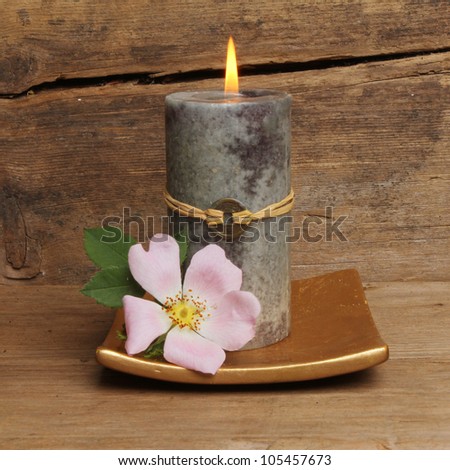 Wild dog rose and burning Feng Shui candle against a background of old cracked and weathered wood