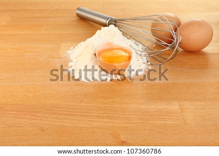 Flour with an egg yolk, eggs and a whisk on wooden worktop