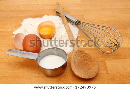 Baking ingredients, flour, egg and sugar with a wooden spoon and whisk on a kitchen worktop