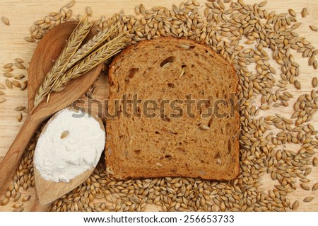 Slice of multi seeded brown bread on a wooden board with barley grains and ears of barley and flour in wooden spoons