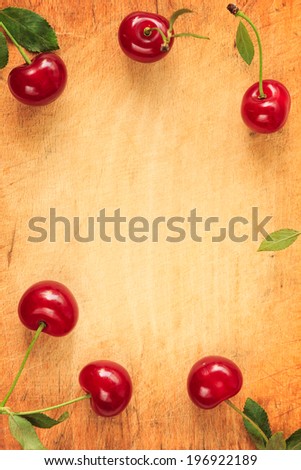 Red cherries frame/ border. Red cherries on a wooden background. Central copy space.