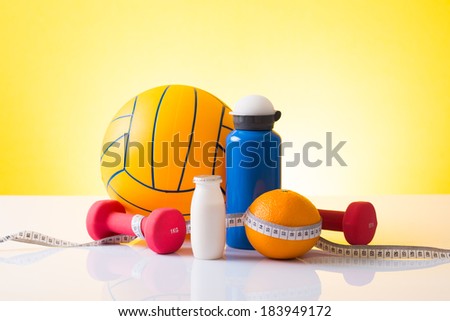 Fitness; Volleyball, sport bottle, pink dumbbells and orange wrapped with measuring tape on yellow background;