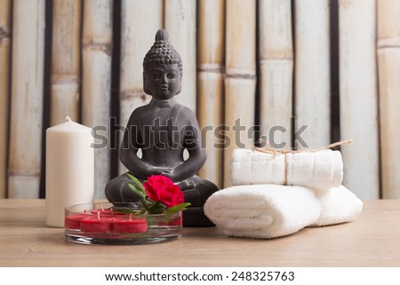 Buddha statue, white candle, white towels with red rose on bamboo background