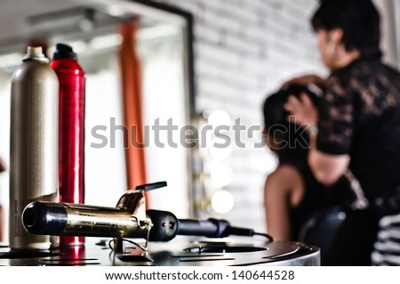 Hairspray and curling iron on the bottom left of the frame and the stylist and client blurred in the background